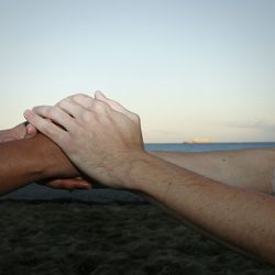 Close-up of hands on sand at beach against sky