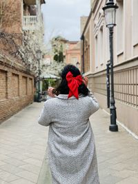 Rear view of woman walking on footpath amidst buildings in city