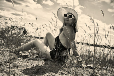 A woman in a swimsuit, hat and sunglasses sunbathes in summer on the riverbank among the grass