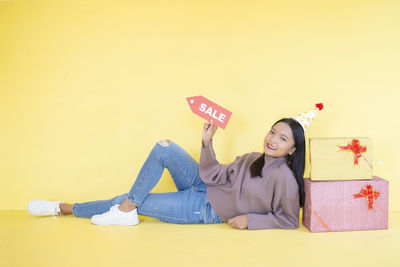 Young woman lying on wall against yellow background