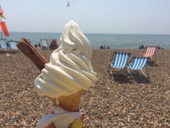 Cropped hand holding ice cream cone at beach on sunny day