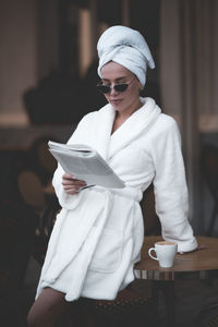 Woman wearing bathrobe reading magazine standing at cafe