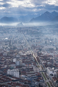 Aerial view of city buildings against mountains and cloudy sky