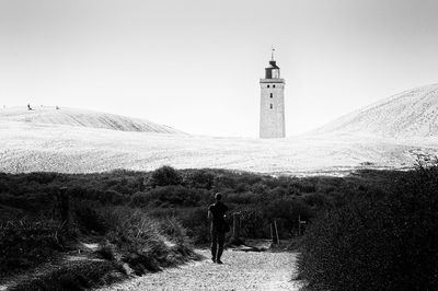 Rear view of man standing on field by rubjerg knude lighthouse against sky