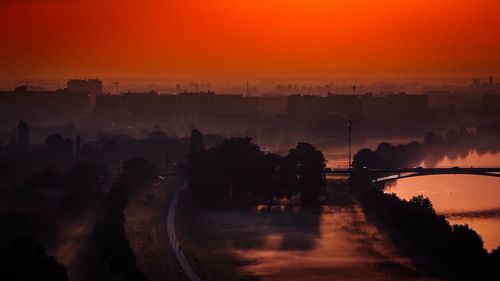 Silhouette city by river against orange sky