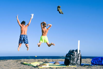 People jumping on beach against clear blue sky