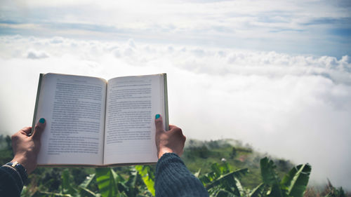 Cropped hand of woman holding book against sky