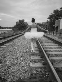 Full length rear view of ballerina walking on railroad track against sky