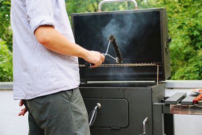 Midsection of man cleaning barbecue grill with wire brush