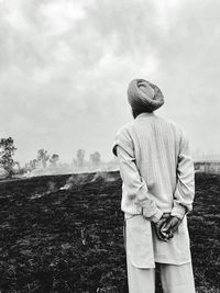 Rear view of man standing on burnt field against sky