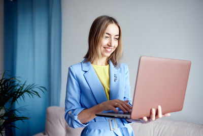 Portrait of young businesswoman using laptop while sitting on bed at home
