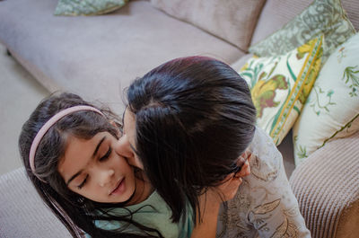 High angle view of woman kissing daughter on sofa at home