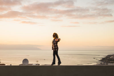 Rear view of woman standing at beach against sky during sunset