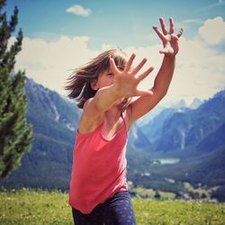 Girl with arms outstretched running on grassy field against mountains