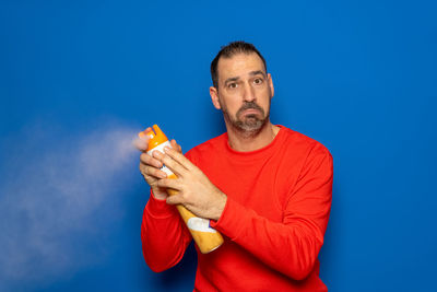 Portrait of young woman holding bottle against blue background