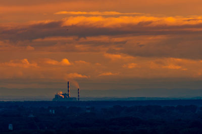 Silhouette factory against sky during sunset