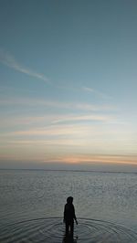 Silhouette woman standing at beach against sky during sunset