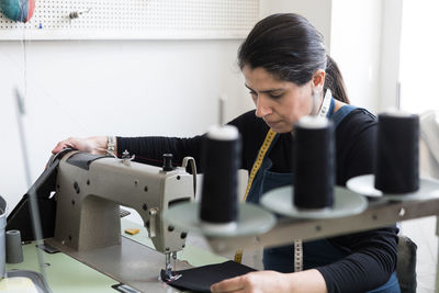 Mature female tailor sewing fabric with machine at laundromat