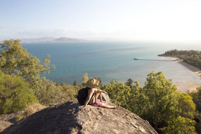 Backpacker with hat and swimsuit, on top of rocky hill during sunset