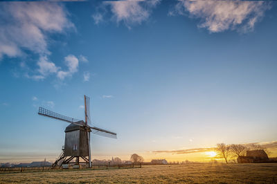 Traditional windmill on field against sky during sunset