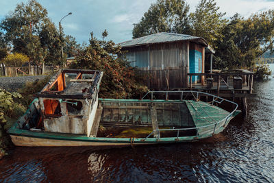 Abandoned boat moored by trees against sky