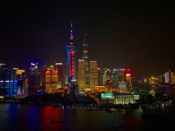 Illuminated buildings by river against sky at night