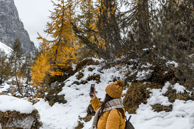 Side view of young woman hiking on snowy path, taking photos of mountains