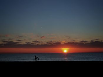 Silhouette person on beach against sky during sunset