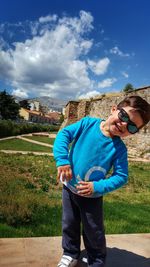 Portrait of smiling boy standing on field against cloudy sky