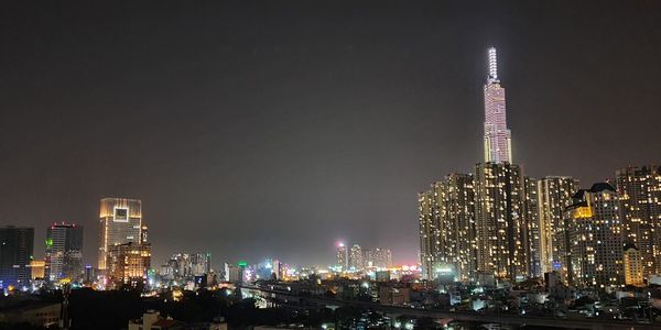 Illuminated modern buildings in city against sky at night