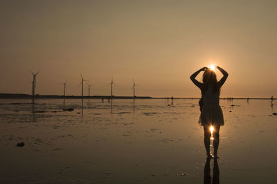 Woman standing on beach against sky during sunset