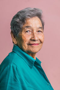 Side view of elderly female with short gray hair and brown eyes looking at camera on pink background in studio