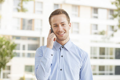 Portrait of smiling man standing on mobile phone in city