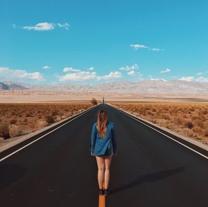Rear view of girl standing on road against blue sky
