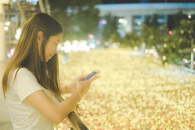 Side view of young woman using mobile phone outdoors