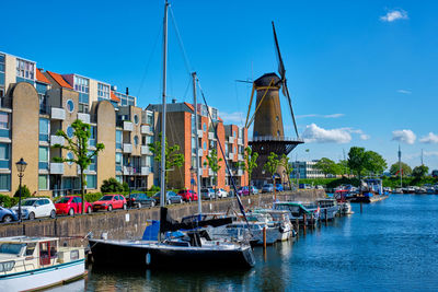 Sailboats moored on river by buildings against sky