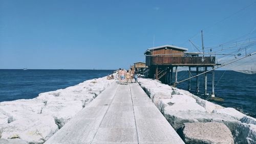 People on jetty by sea against clear blue sky