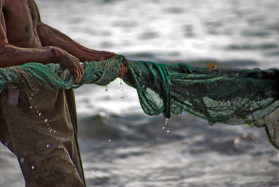 Midsection of fisherman holding fishing net by sea