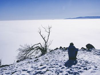 Rear view of man sitting on snowcapped landscape against sky