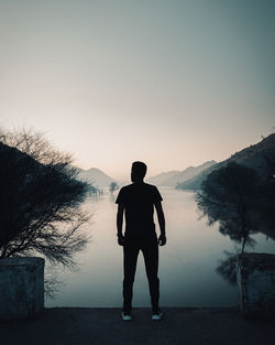 Rear view of man standing on by lake against sky