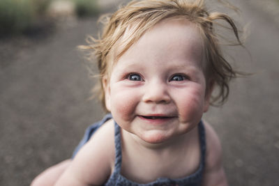 Close-up portrait of cute smiling baby girl sitting on road in forest