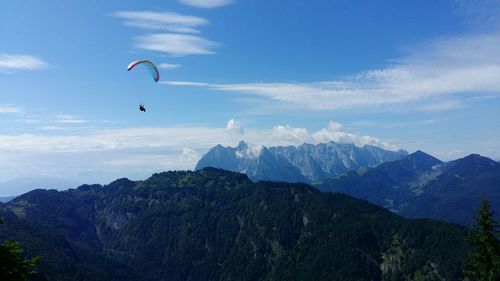 Distant view of person paragliding over mountains against blue sky