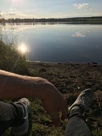 Low section of man relaxing by lake against sky