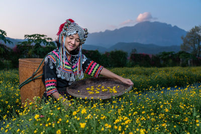 Smiling woman in traditional clothing holding wicker basket while standing in farm