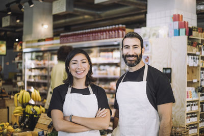 Portrait of smiling multiracial male and female retail clerks wearing aprons standing at grocery store