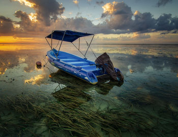 Fishing boat moored on sea against sky at sunset