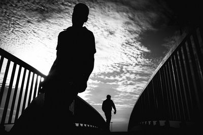 Silhouette men on railing against sky