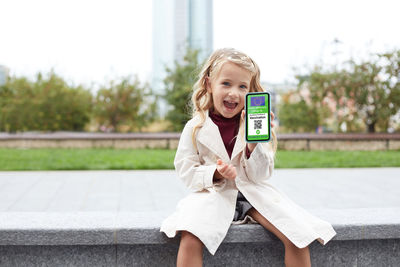 Smiling girl showing smart phone while sitting outdoors