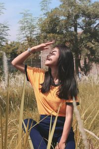 Young woman shielding eyes while sitting on grass