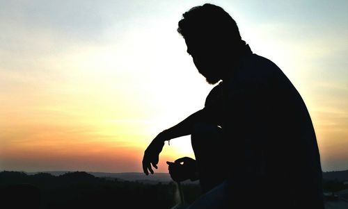 Silhouette man with arms outstretched against sunset sky